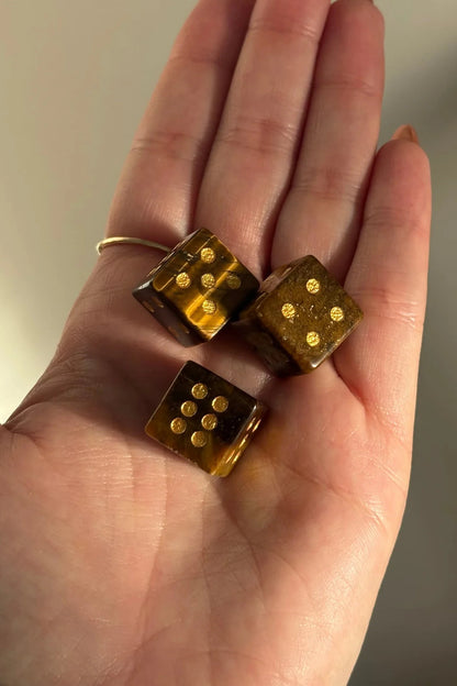 Three small translucent amber dice with gold-colored pips resting on an open hand.
