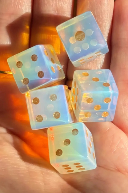 Five translucent light blue dice with embedded gold glitter, resting in the palm of a hand.