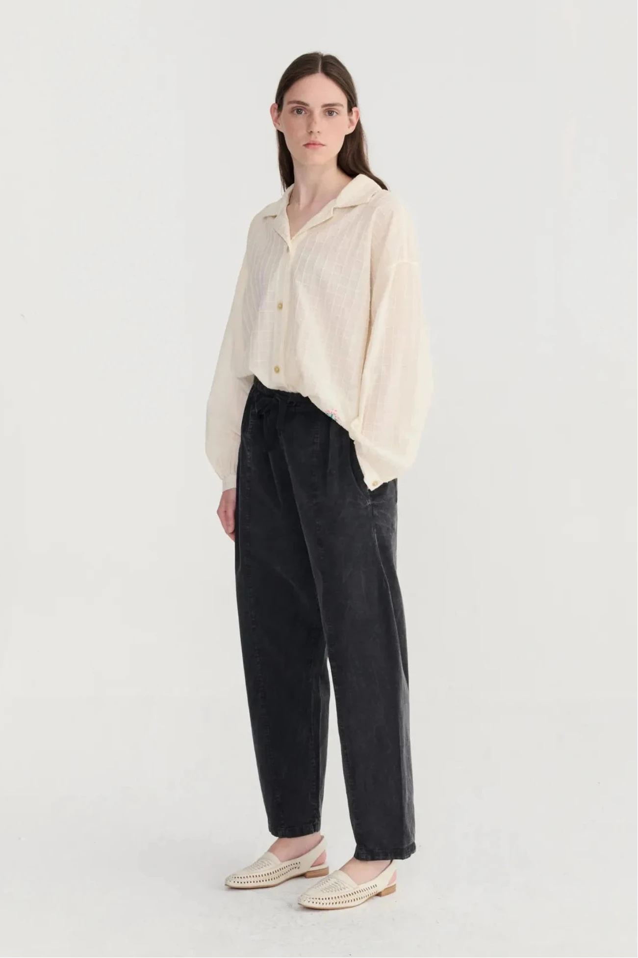 Woman wearing a cream blouse and black pants on a white background