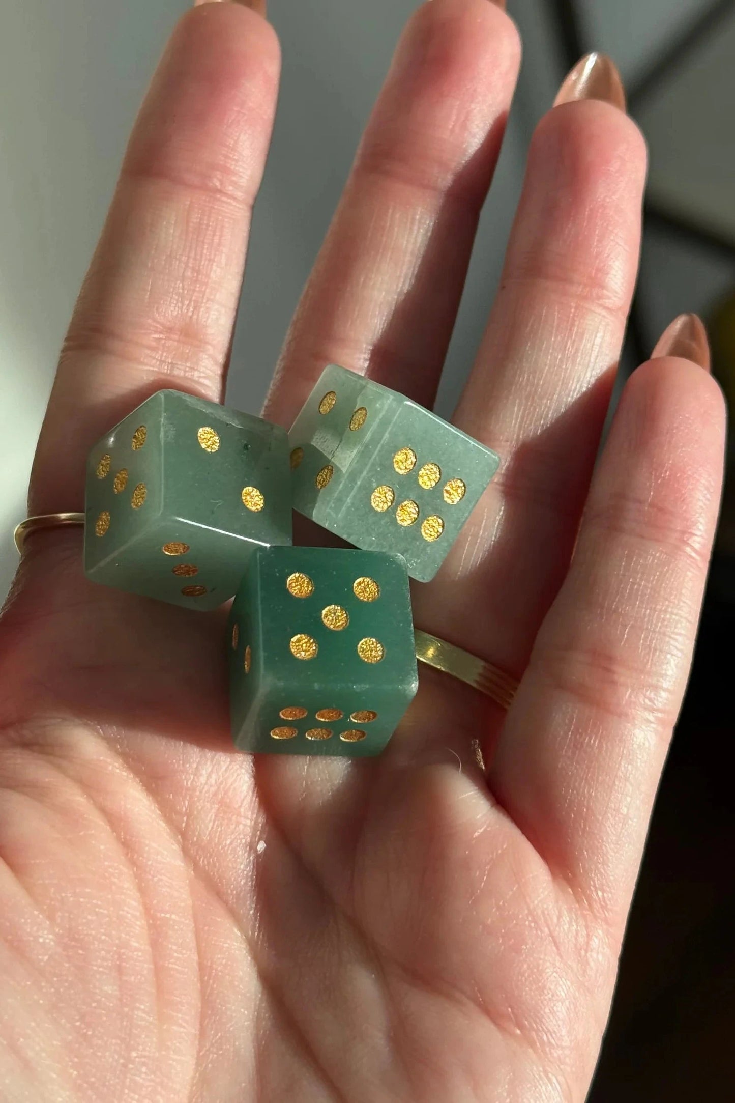 Three translucent green dice with gold dots resting on an open hand, with a gold ring on the ring finger.