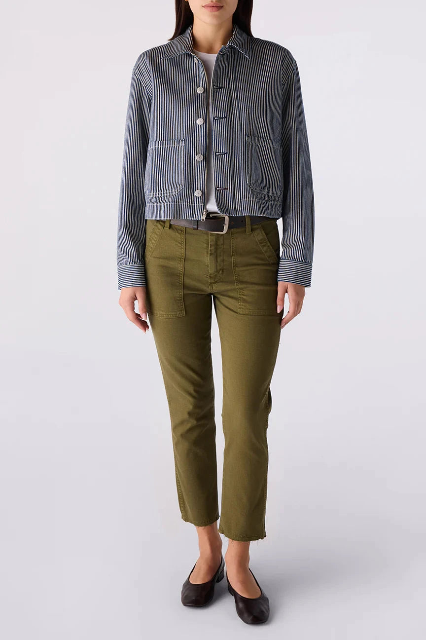 A model wearing a cropped, blue-gray vertically striped button-up shirt jacket, olive green cropped trousers, and black flats, photographed against a light gray studio background.