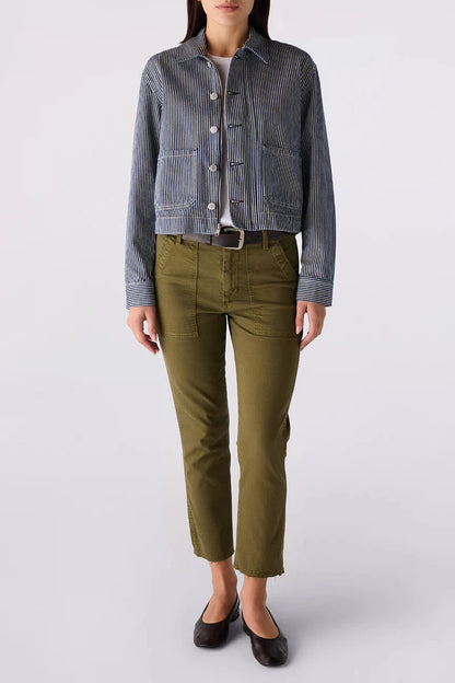 A model wearing a cropped, blue-gray vertically striped button-up shirt jacket, olive green cropped trousers, and black flats, photographed against a light gray studio background.