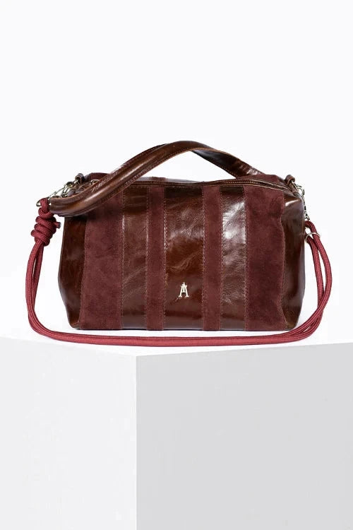 A dark reddish-brown leather handbag with a top handle and shoulder strap, displayed on a white pedestal against a white background.