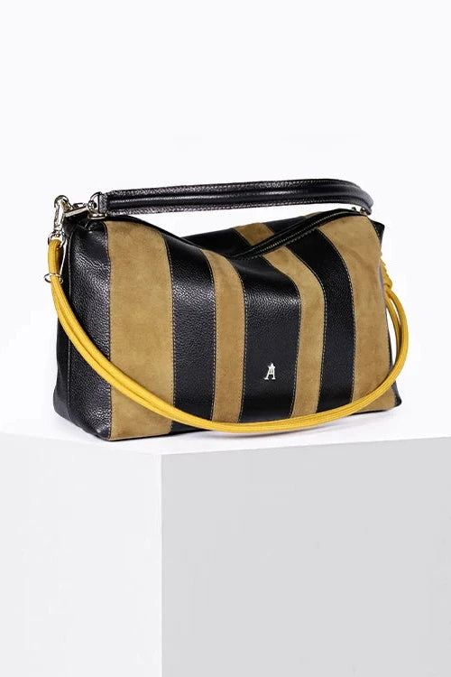 A striped leather shoulder bag with black and tan vertical stripes, a black top handle, and a bright yellow shoulder strap, displayed on a white pedestal against a white background.