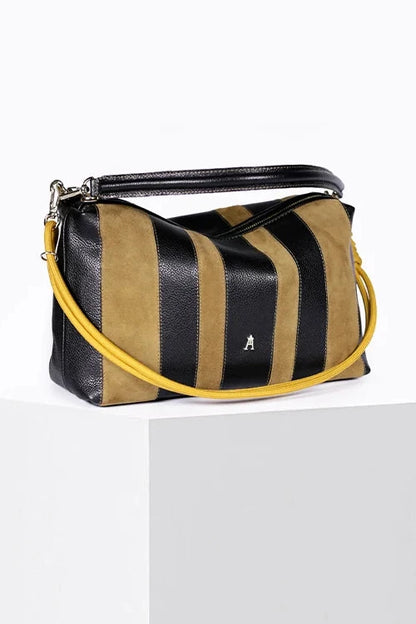 A striped leather shoulder bag with black and tan vertical stripes, a black top handle, and a bright yellow shoulder strap, displayed on a white pedestal against a white background.