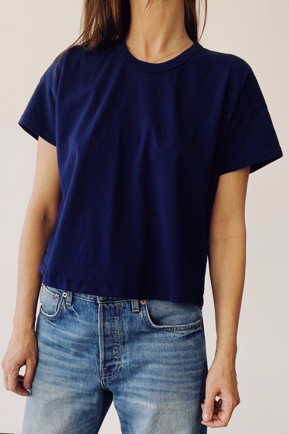 Person wearing a navy blue t-shirt and light blue jeans against a plain background