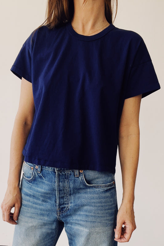Person wearing a navy blue t-shirt and light blue jeans against a plain background