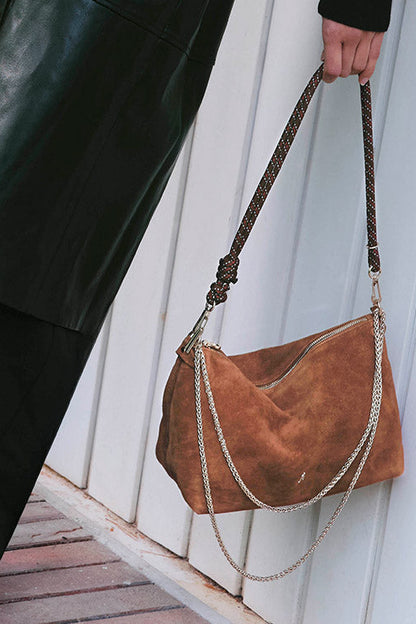 Brown suede handbag with braided handle held by a person against a white wooden background